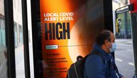 A commuter boards a bus near an advertisement showing that the Local Covid-19 Alert Level is high at a bus stop in London