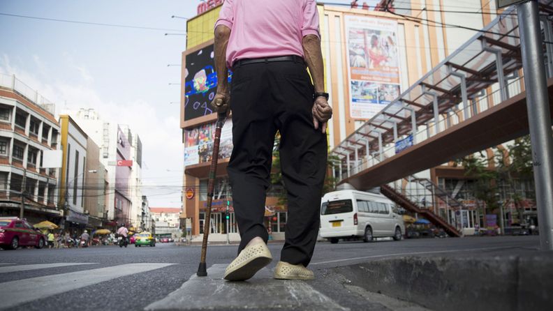 A man uses a walking cane as he walks along a road in the Chinatown area of Bangkok,